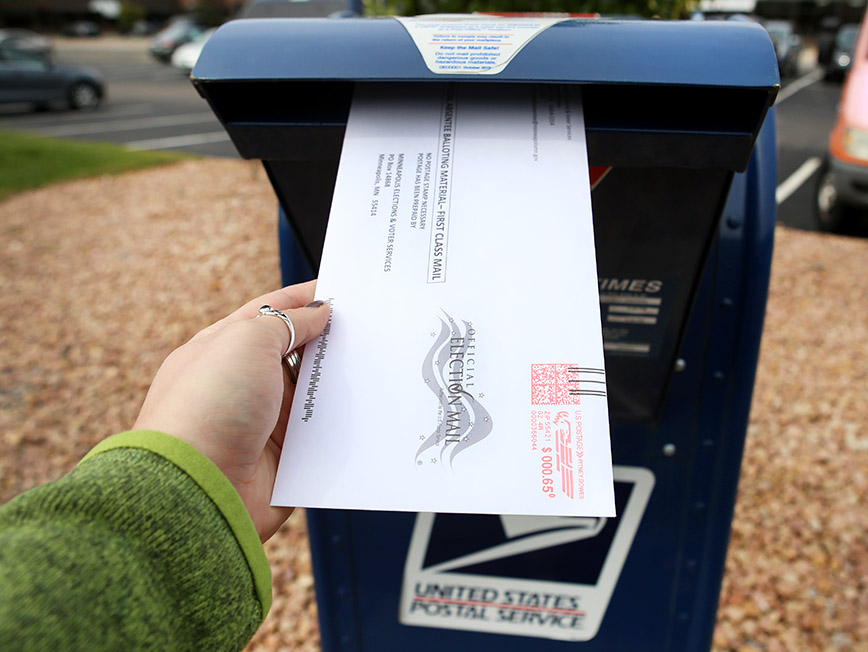 voter putting their absentee ballot into a mailbox